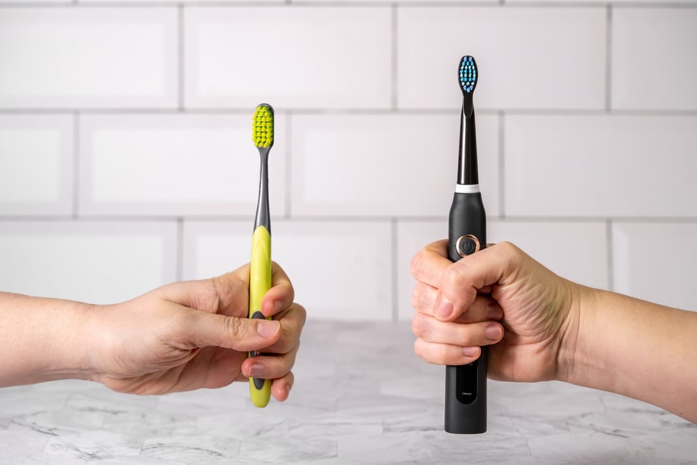 Deux mains tenant respectivement une brosse à dents manuelle et une brosse à dents électrique
