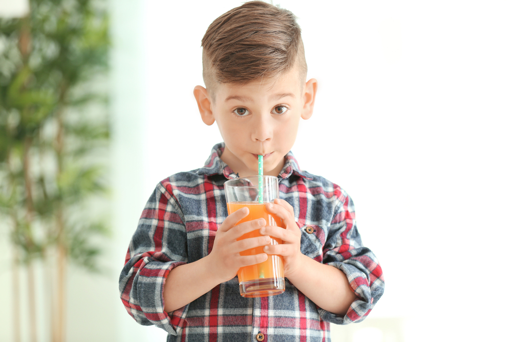 Enfant qui boit un jus de fruits, une boisson nocive pour la santé buccodentaire.