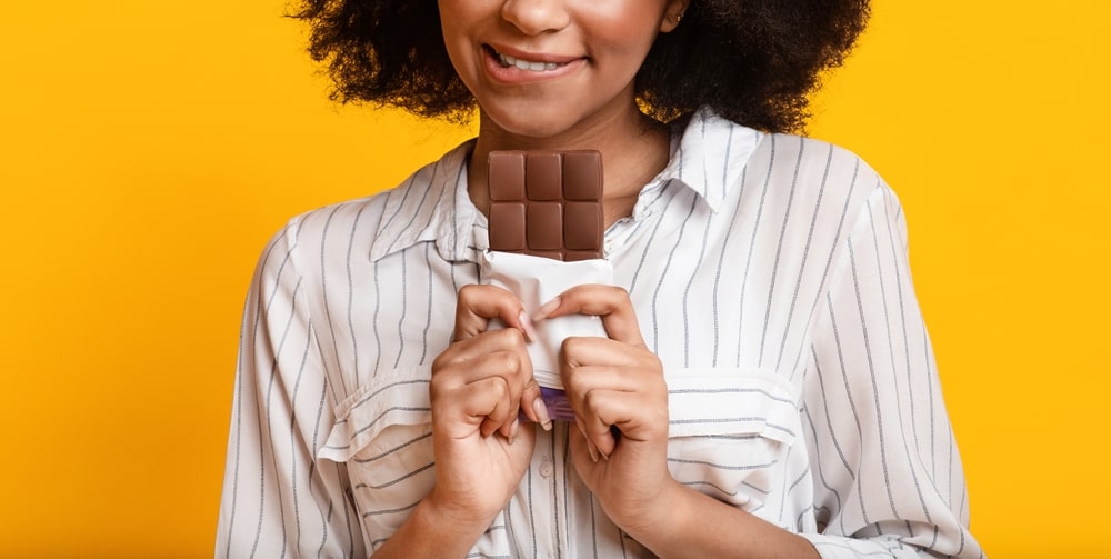 Femme dont on voit le bas du visage et la barre de chocolat qu'elle s'apprête à manger